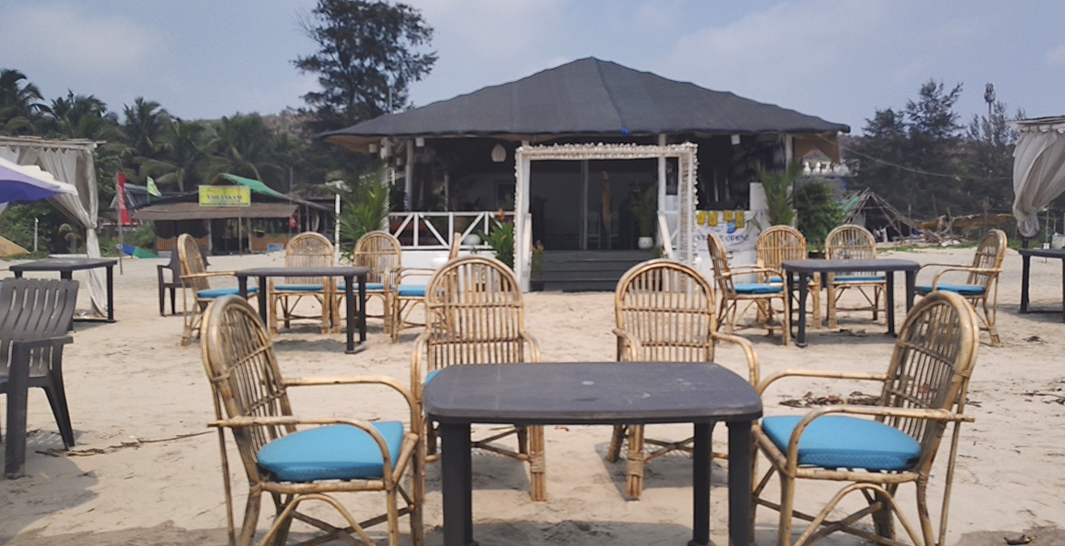 Outdoor beachside restaurant and dining setup at Morjim Beach in Goa with tables, chairs, and sandy seating area