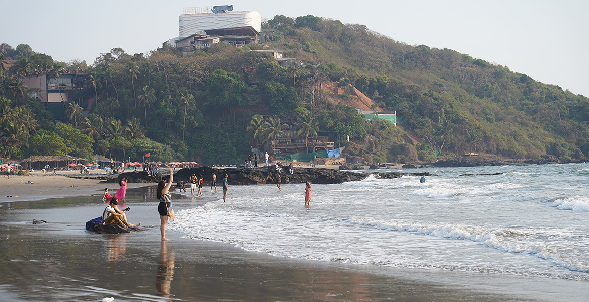 People enjoying the shoreline and sea waves at Ozran Beach in Goa with hillside backdrop