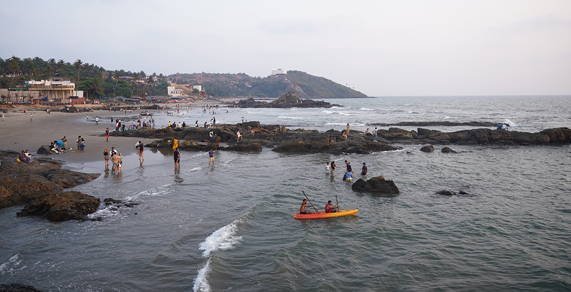People exploring the rocky shoreline and sea view at Ozran Beach in Goa