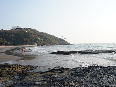 Rocky shoreline and coastal view at Ozran Beach in Goa with hillside backdrop