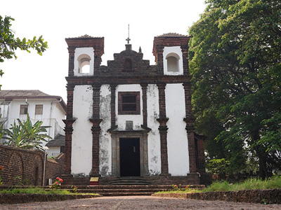 Front view of the historic Se Cathedral church in Old Goa surrounded by trees and stone pathways