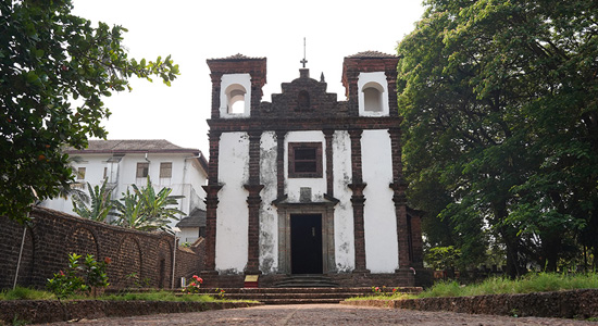 Front view of the historic Se Cathedral church in Old Goa surrounded by trees and stone pathways