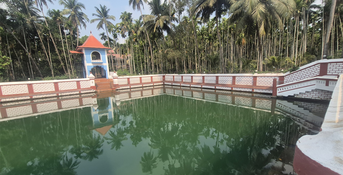 Sacred temple tank at Shri Nageshi Temple in Bandora, Goa surrounded by coconut palms and traditional temple architecture