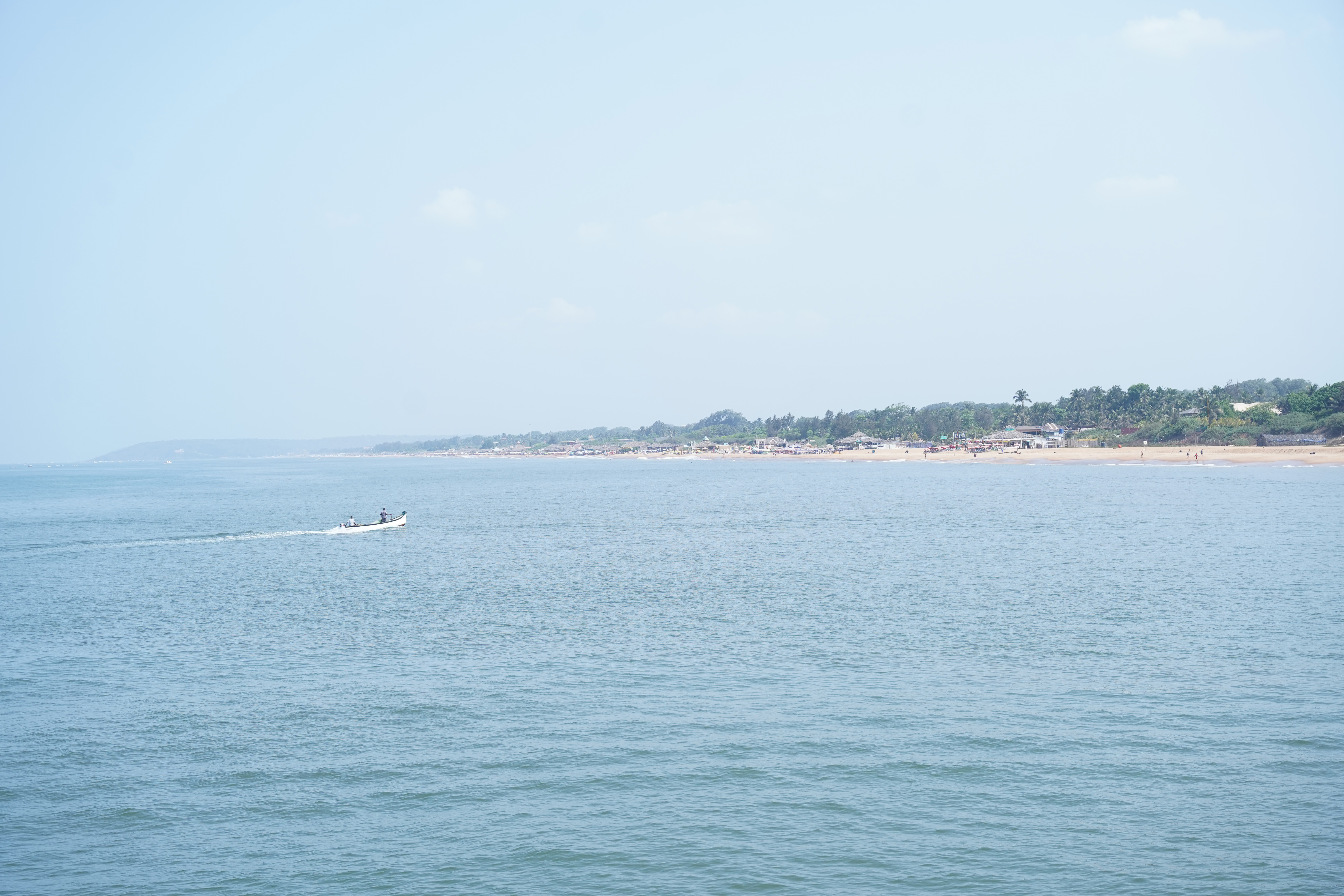 Wide coastal view of Sinquerim Beach in Goa with calm sea waters and a small fishing boat