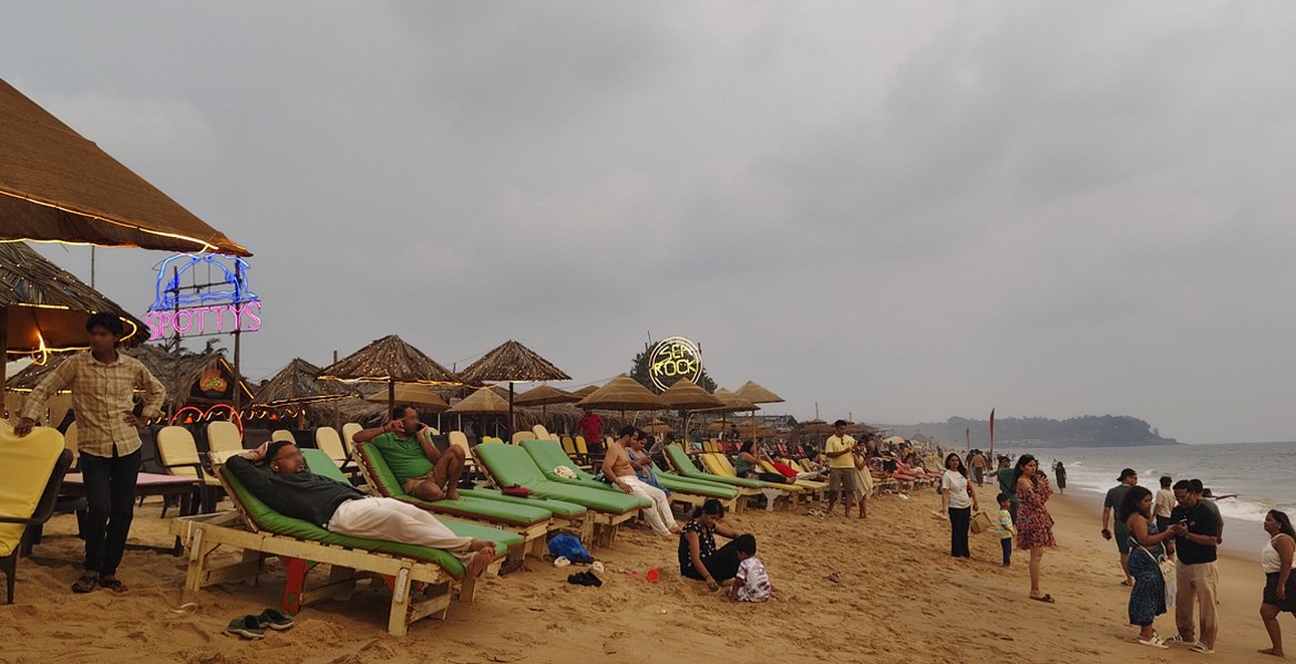 Sunset beach shacks in Goa with sun loungers, thatched umbrellas, seaside restaurants and visitors along the sandy beach
