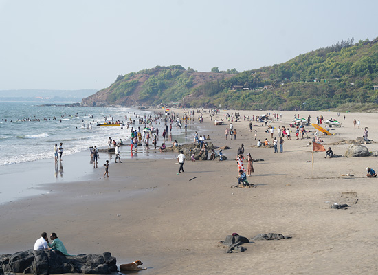 Crowded view of Vagator Beach in Goa with visitors along the shoreline, sea waves, and green hills in the background