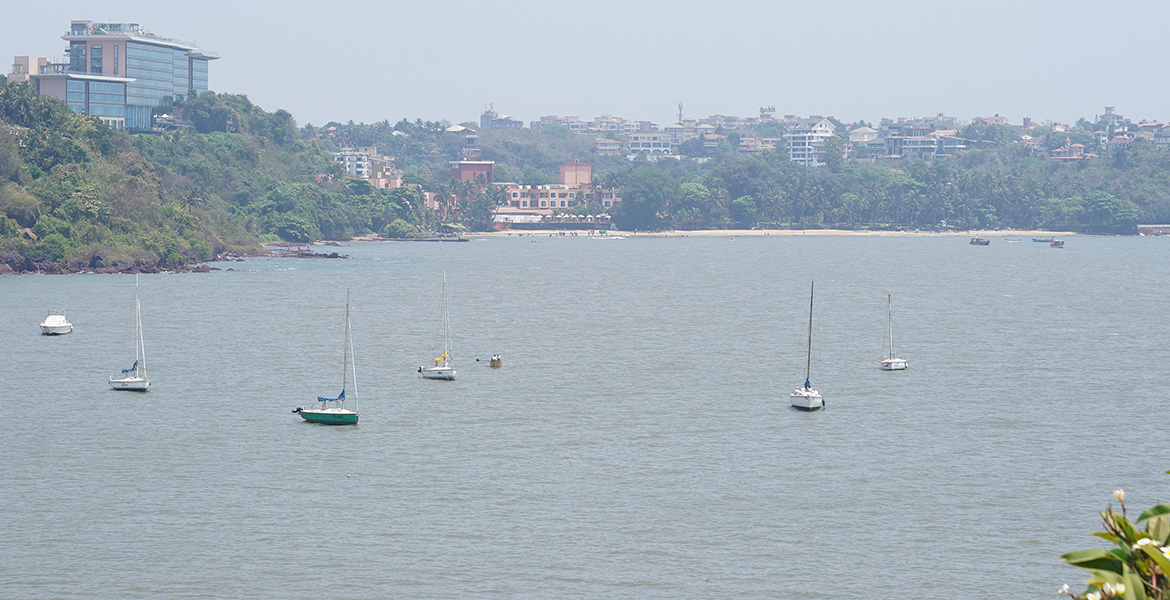 Scenic view of Vainguinim Beach in Goa with anchored boats, calm water, and coastal greenery in the background