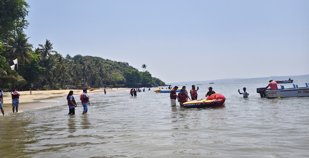 Visitors enjoying water activities and inflatable rides at Vainguinim Beach in Goa with palm trees and calm shoreline views