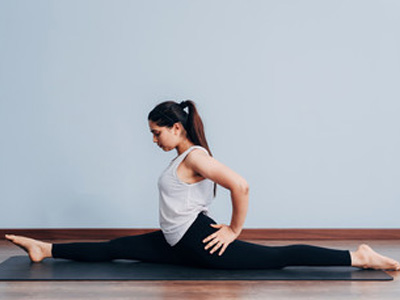 Woman practicing yoga split pose indoors on a yoga mat
