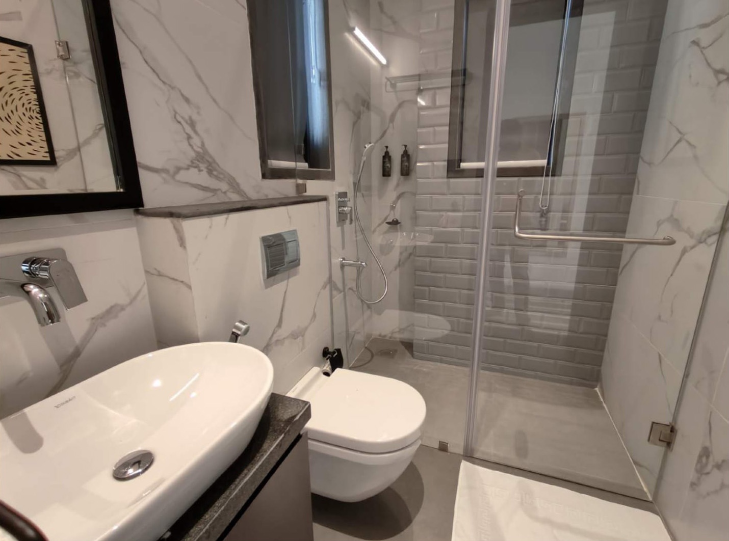 Modern bathroom with marble walls, vessel sink, and glass shower enclosure.