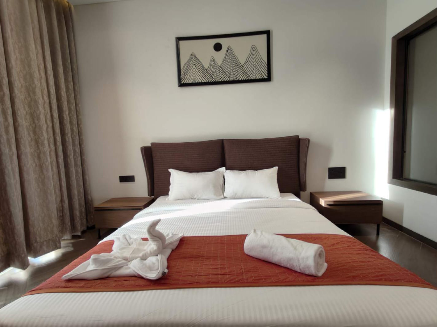 Bedroom with white linens, an orange runner, and mountain artwork.