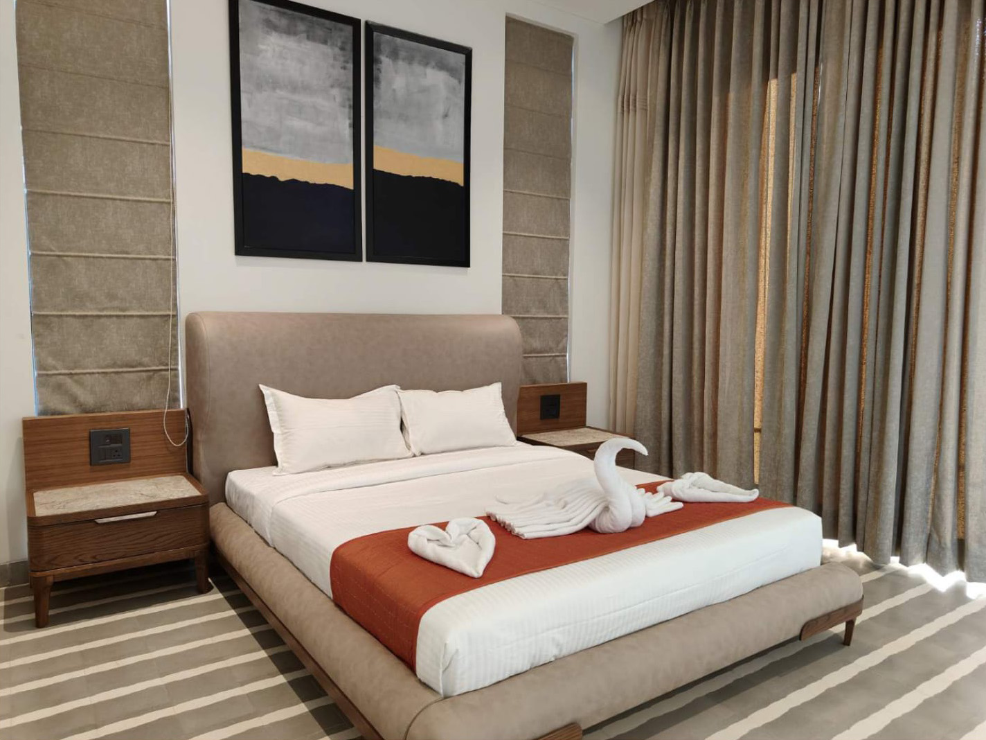 Bedroom featuring a light upholstered bed and two dark, abstract landscape paintings.