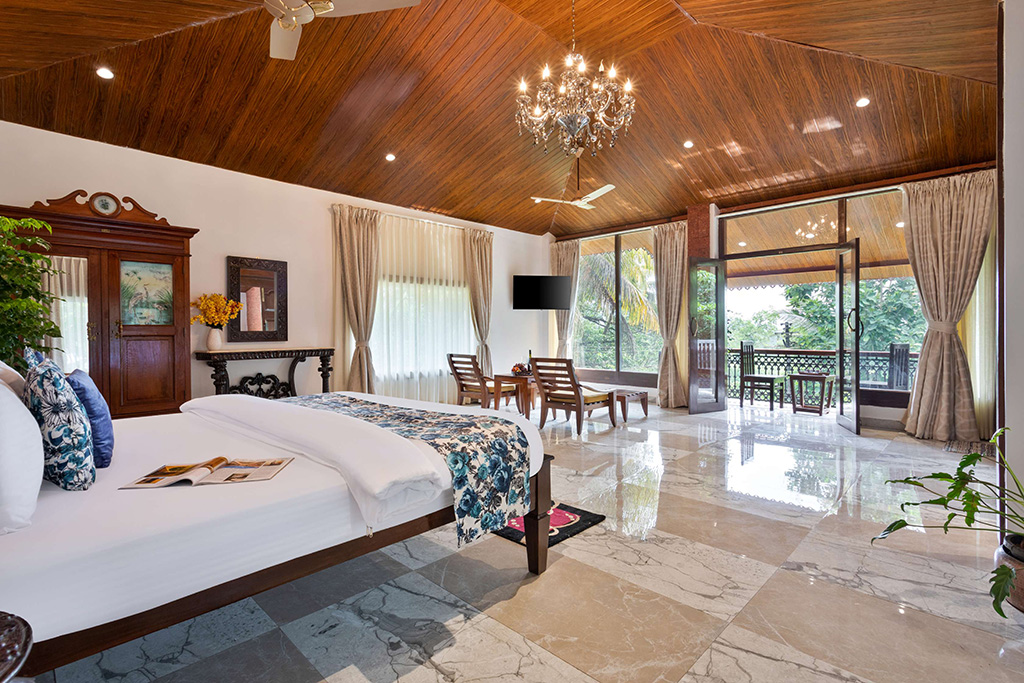 Room with white bed, high wood-paneled ceiling, and balcony view