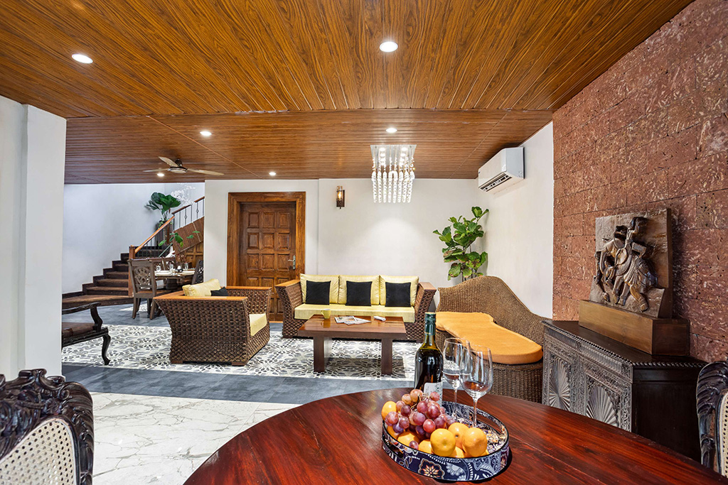 Living area with wicker furniture, wood-paneled ceiling, and a staircase in the background