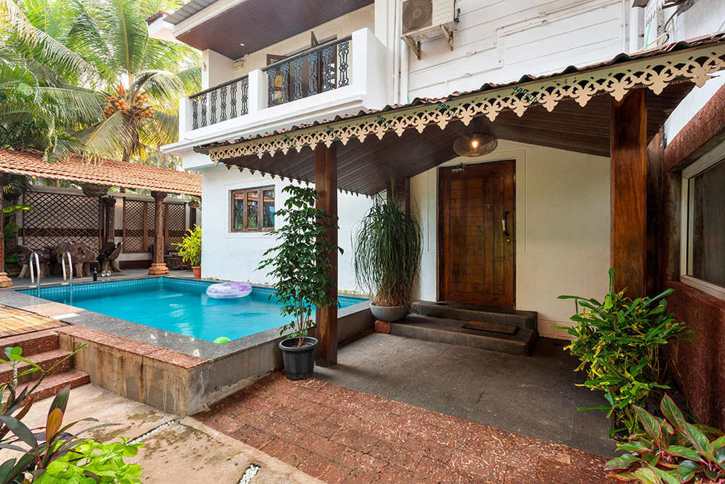 White villa entrance next to a private pool with a covered wooden porch
