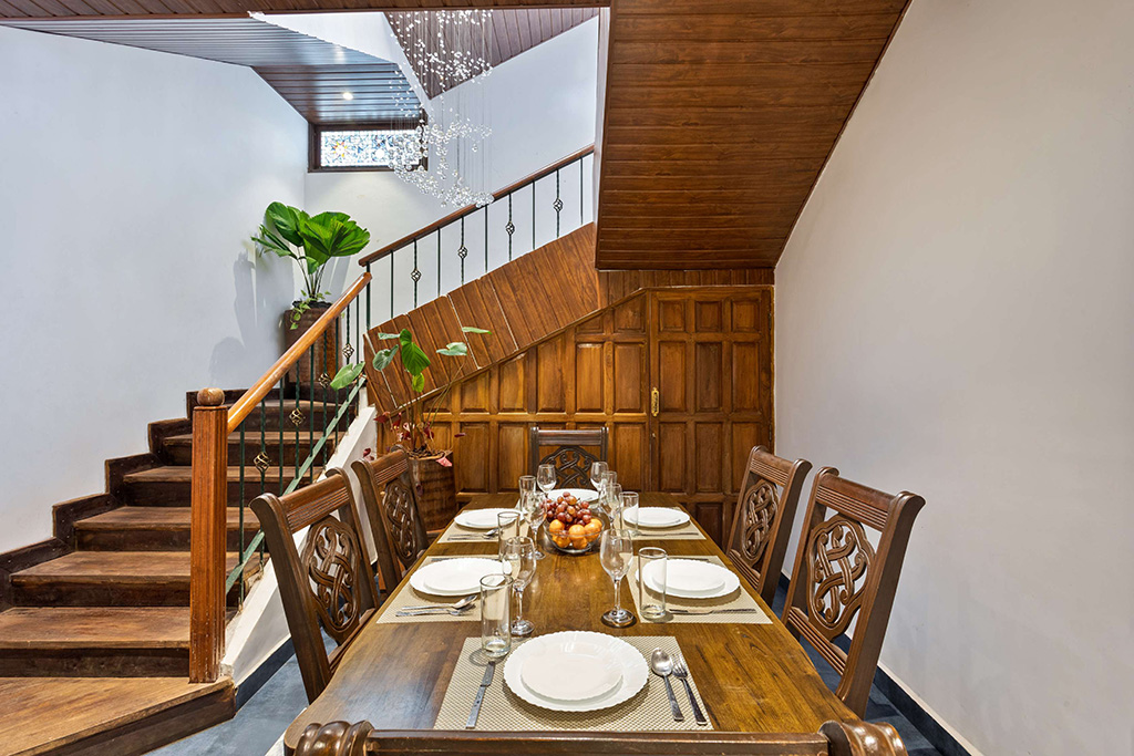 Dining table set for six next to a wooden staircase and paneled wall