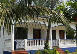 A tropical villa with a white-and-blue exterior, small veranda, and palm trees in the foreground