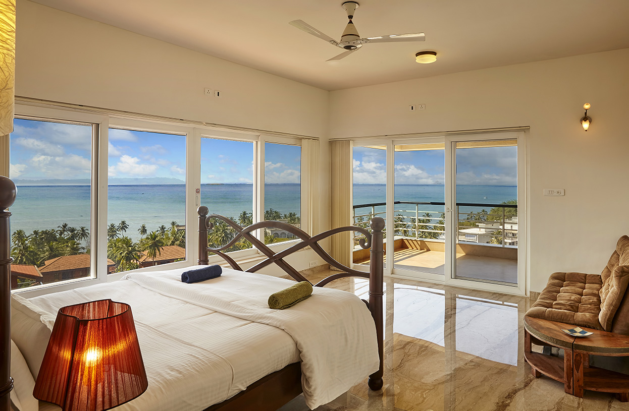 Sea-facing bedroom with balcony access, panoramic windows, and elegant wooden bed at Dolphin Heights