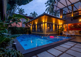 A stylish villa with a private swimming pool illuminated by warm evening lights and surrounded by lush greenery