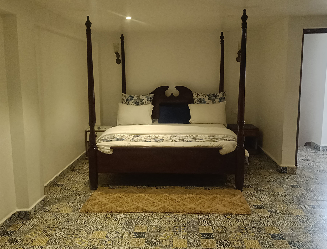 Bedroom with a four-poster bed and patterned tile floor.