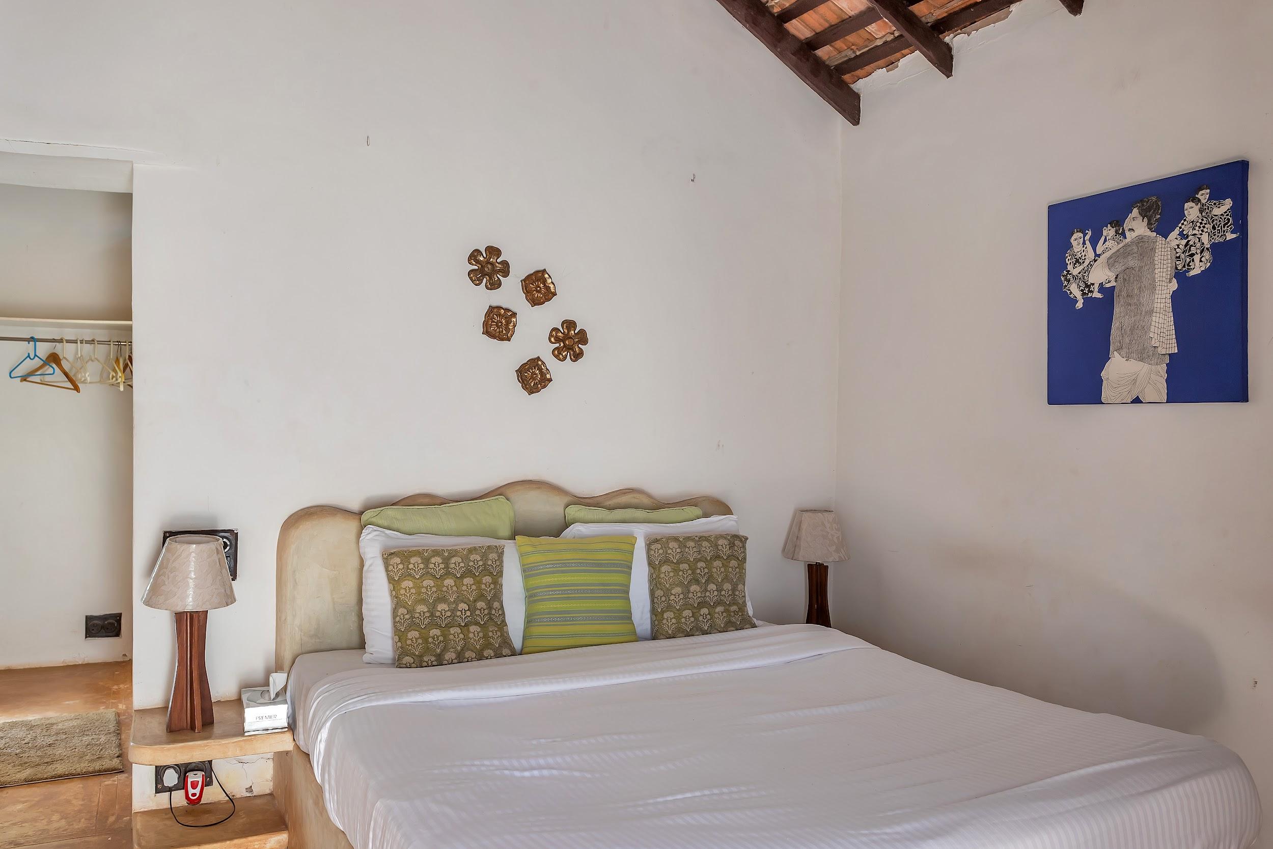 Bedroom with a light headboard, green/yellow accent pillows, and a bright blue artwork