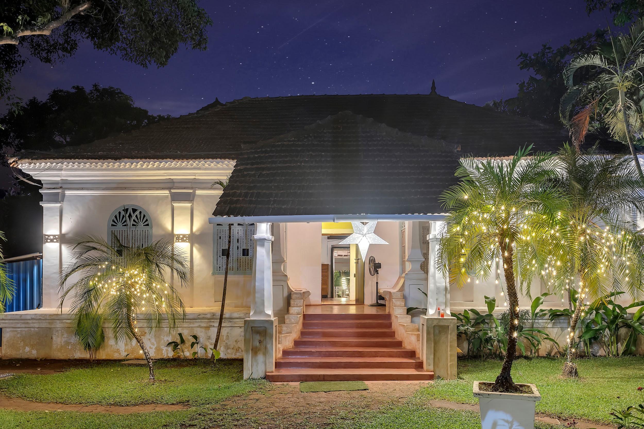 Front exterior of the white Portuguese-style villa at night with illuminated palm trees and a starry sky.