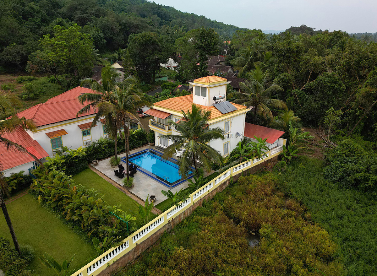 Aerial view of a villa with a pool surrounded by greenery and palm trees