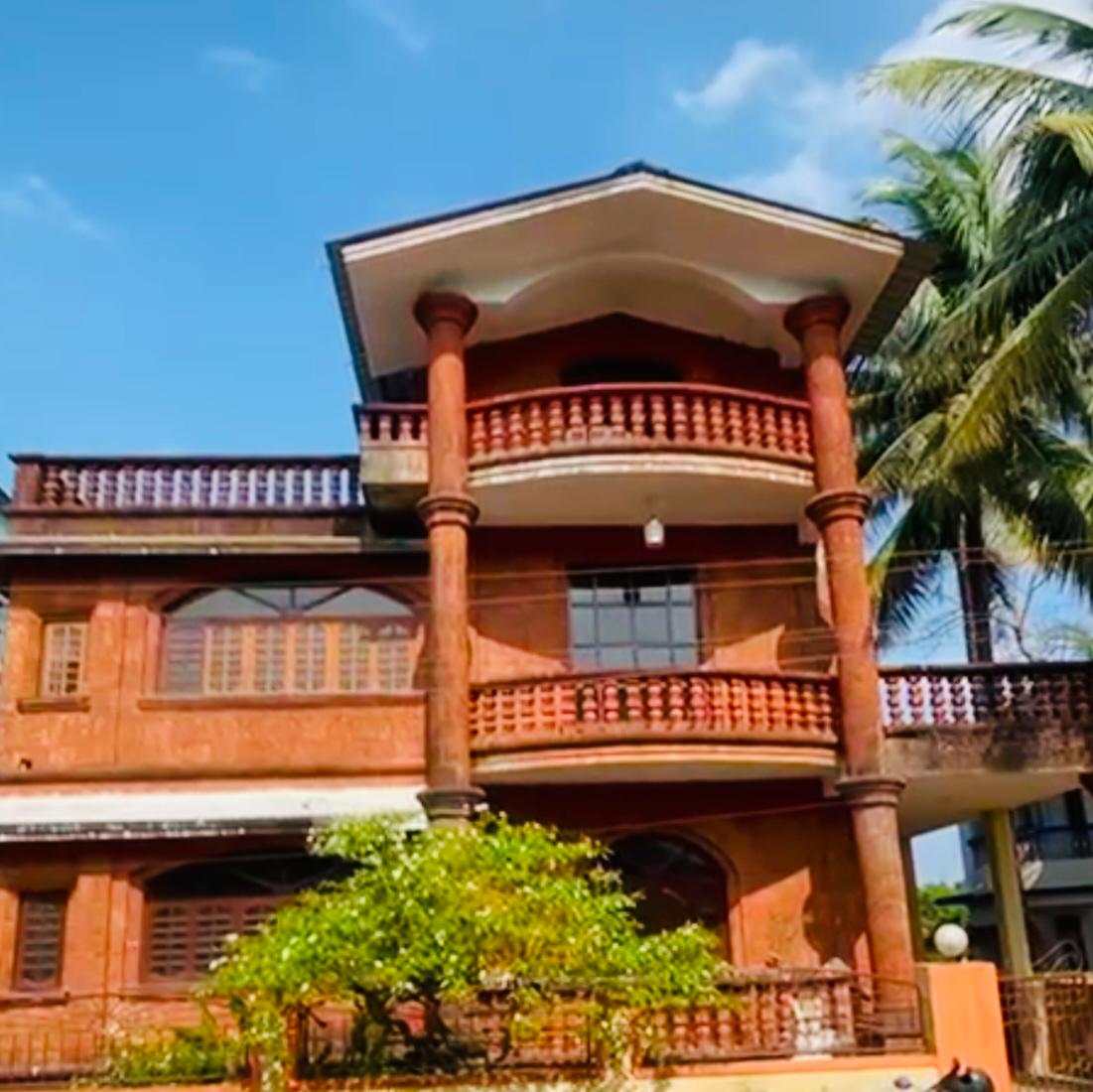 Two-story villa with red brick exterior, balconies, and palm trees nearby