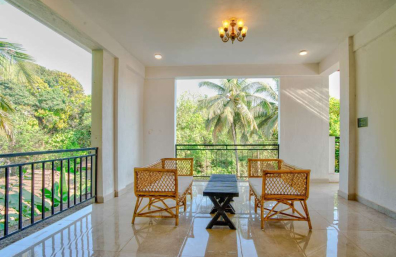 Spacious villa balcony seating area with rattan chairs and tropical palm tree view
