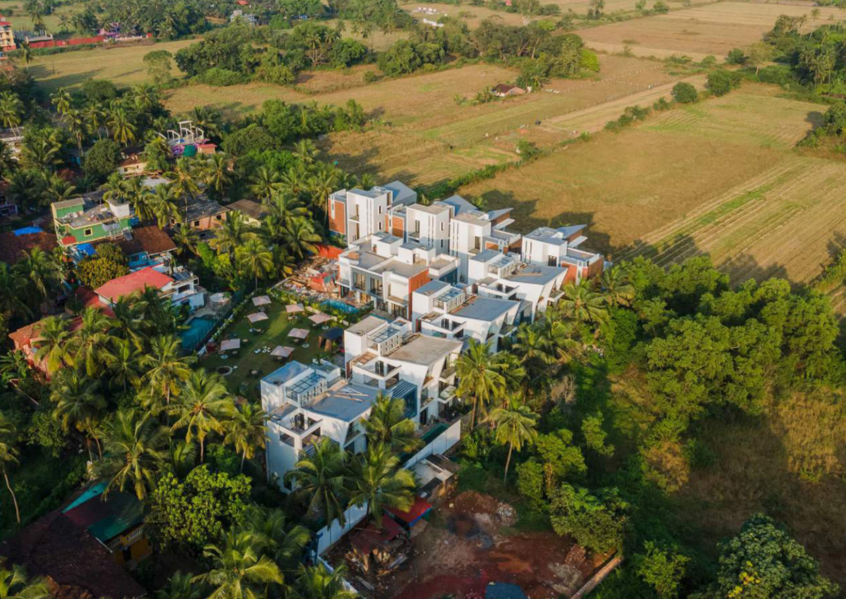 Aerial top view of luxury white pool villa complex surrounded by palm trees and open fields
