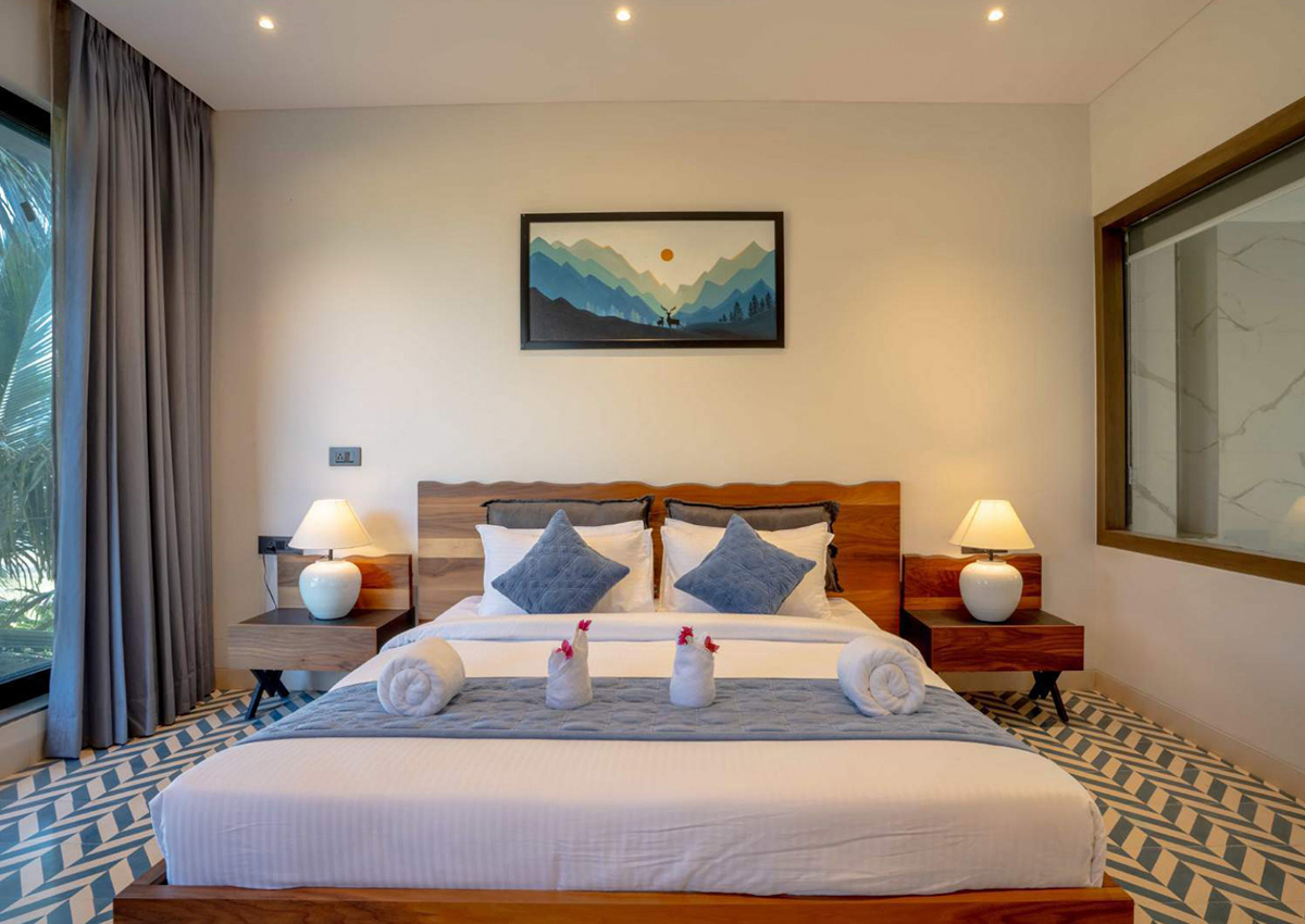 Wide view of king bedroom with blue decor, accent rug, and floor-to-ceiling curtains