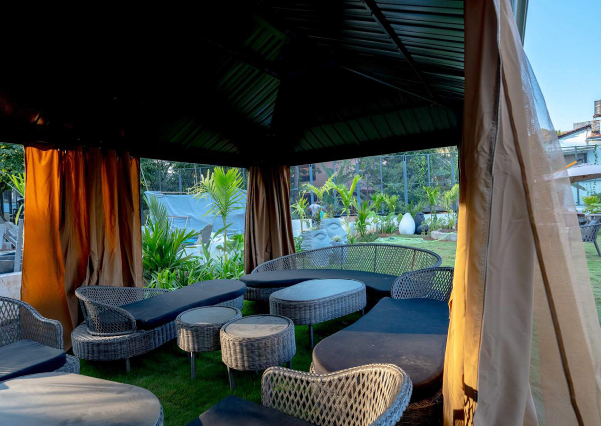 Outdoor gazebo featuring wicker lounge seating surrounded by greenery